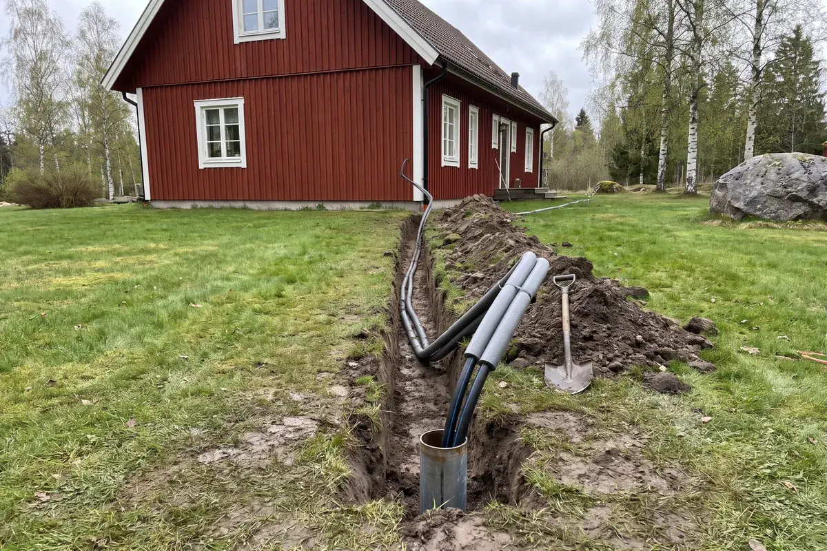 Borrhålets foderrör med två kollektorslangar som leds i ett schakt över gräsmattan fram till ett falurött trähus.