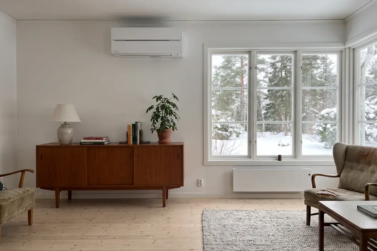 Vit Mitsubishi MSZ-LN Hero-innedel högt på väggen i ett vardagsrum från sjuttiotalet med elradiator under fönstret.