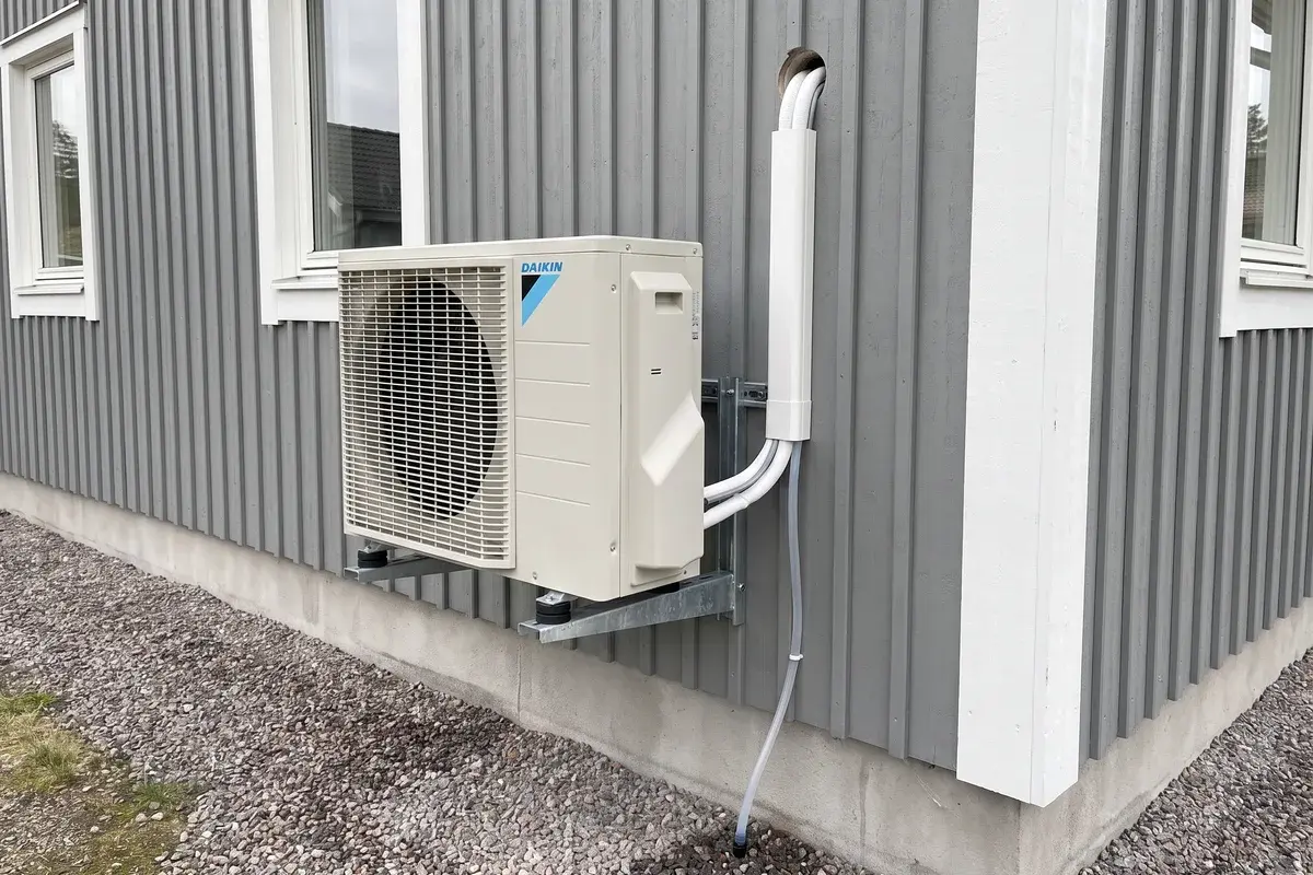 Daikin Perfera-utedel på väggkonsol med vibrationsdämpare, rör i kabelkanal och kondensslang ner i gruset.