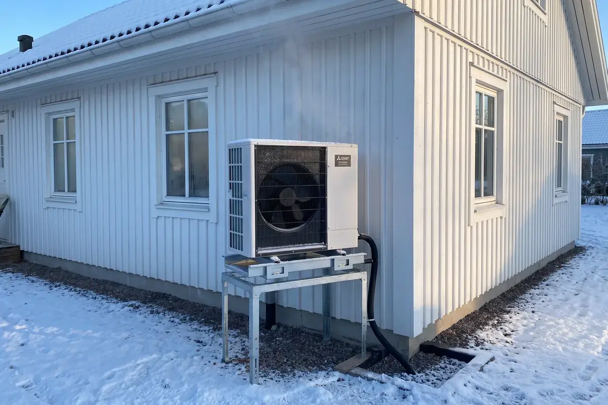 Mitsubishi Ecodan R290-utedel på markstativ med dropptråg och värmd avloppsslang ner i en stenkista i snön.